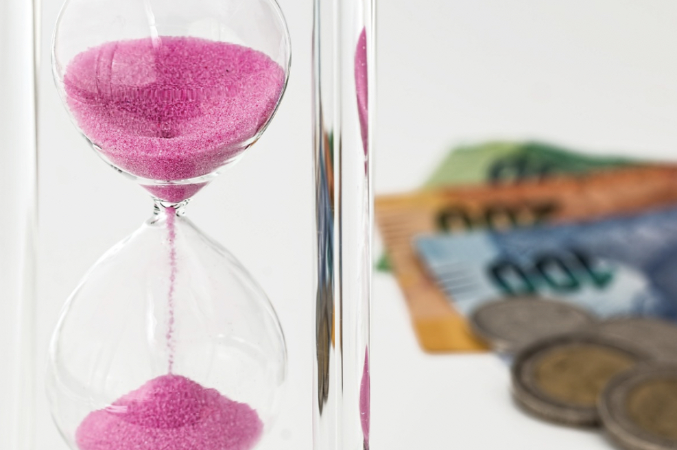 Pink sand hourglass with blurred currency notes and coins in background