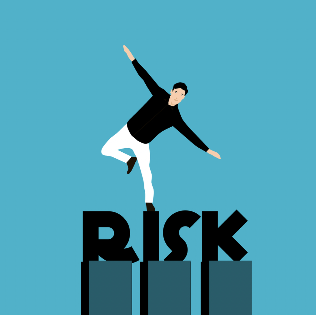 Man Balancing Precariously on the Word 'RISK' Against a Blue Background