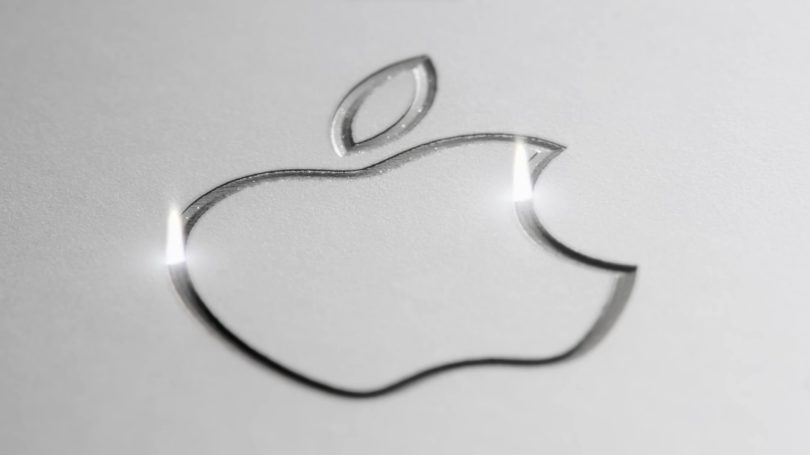 A close-up of the Apple logo embossed on a silver surface with reflective highlights