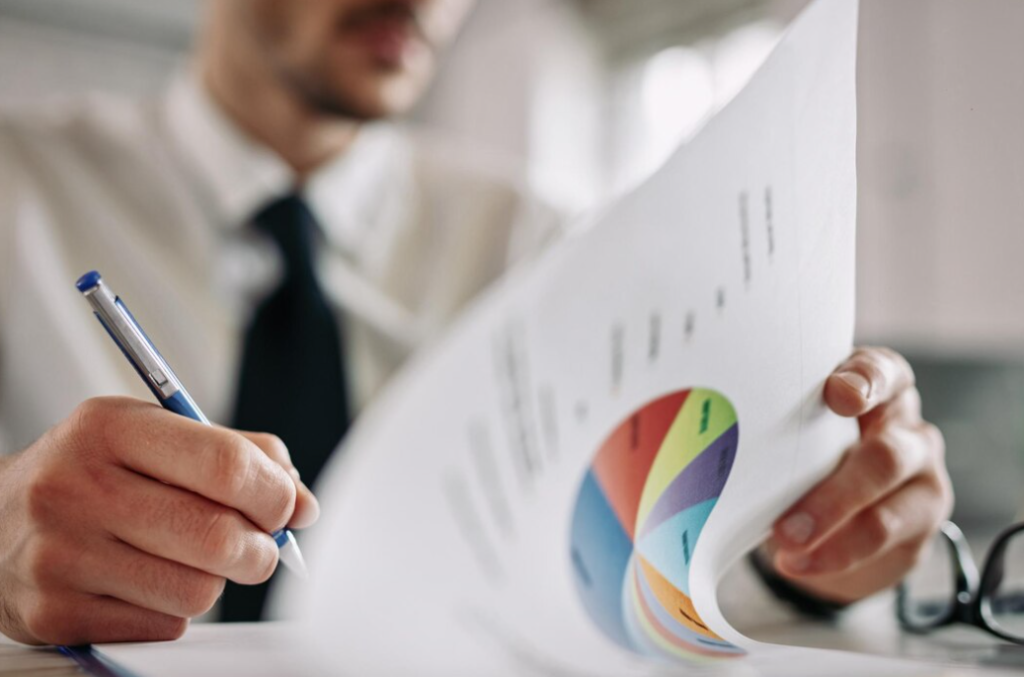 A close look of a man examines a paper with a colorful pie chart, holding a blue pen