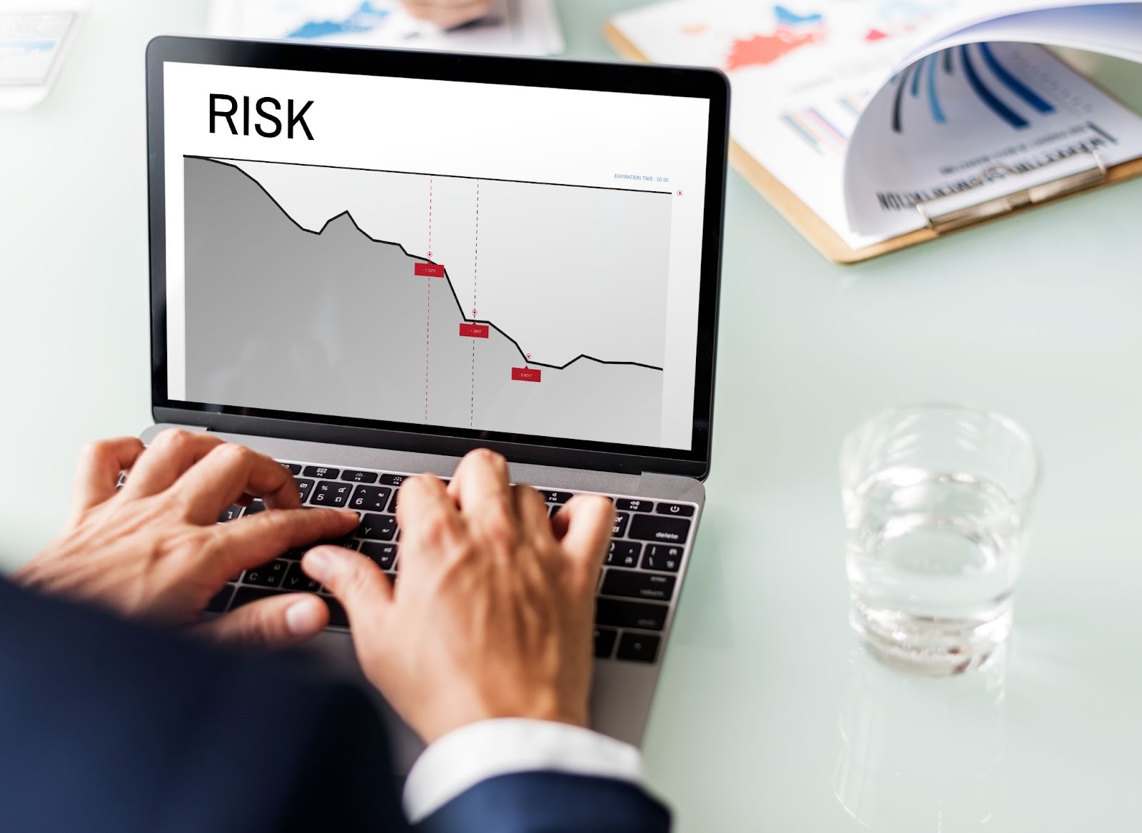 A person typing on a laptop displaying a graph labeled "RISK" with a declining trend line