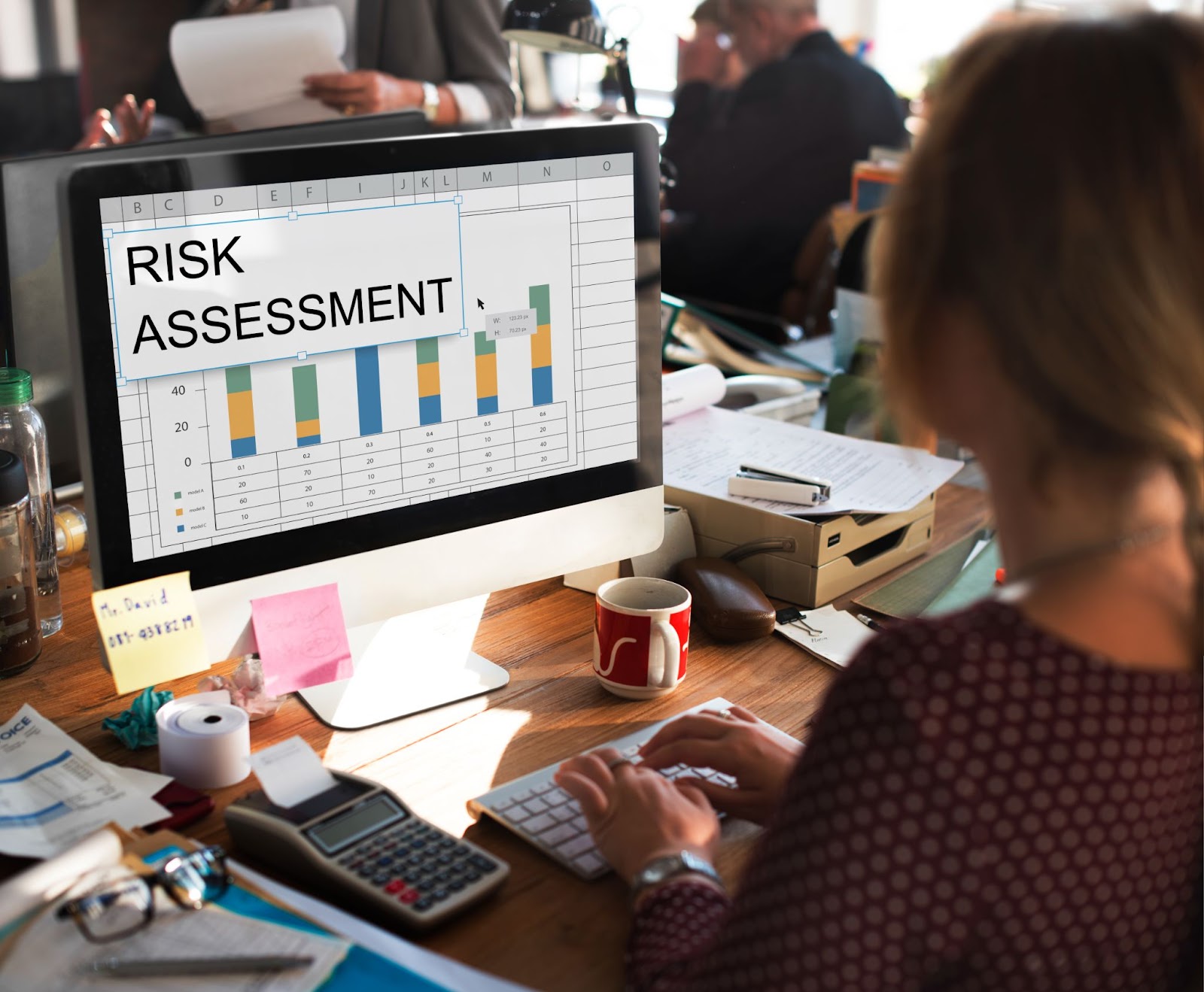 A woman working at a desk with a computer monitor displaying a "RISK ASSESSMENT" bar chart