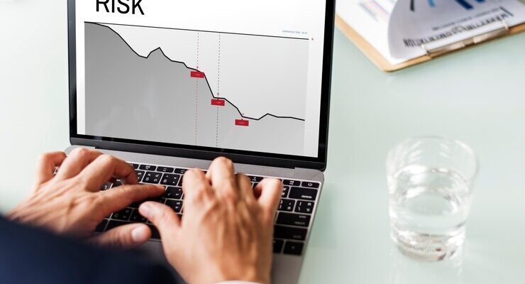 two hands using a laptop with the word “RISK” and a diagram on the screen